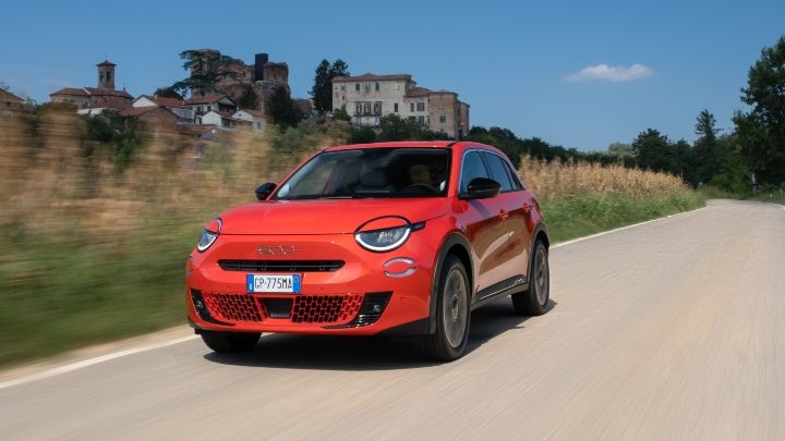 Red Fiat 500 driving past a village