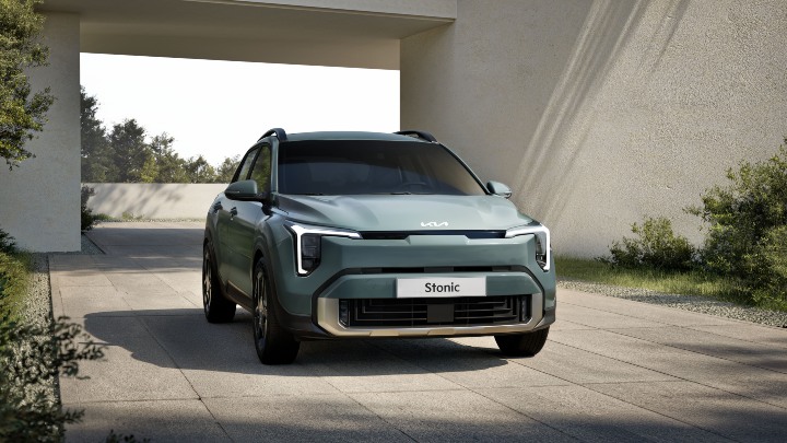 Green Kia Stonic compact SUV shown from the front, parked in a modern outdoor setting