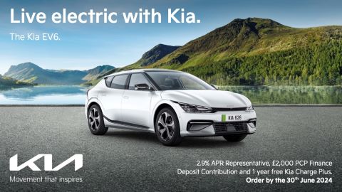 Silver Kia EV6 parked on a beach with mountains to the right side of the image and the ocean on the left side