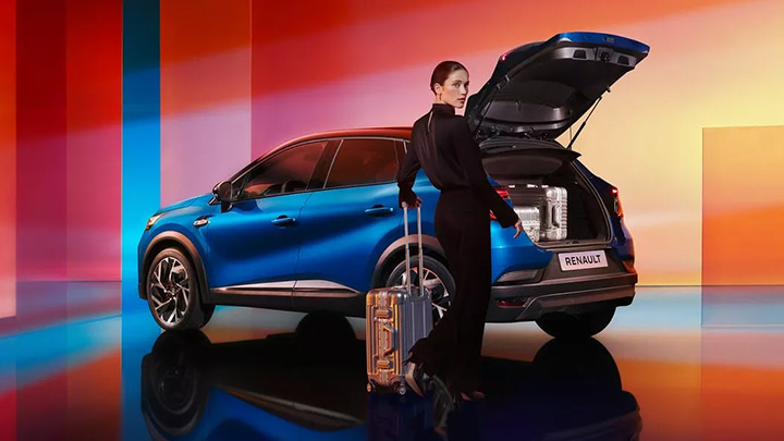 Woman Holding Suitcase Next to Blue Renault Captur With Open Boot 